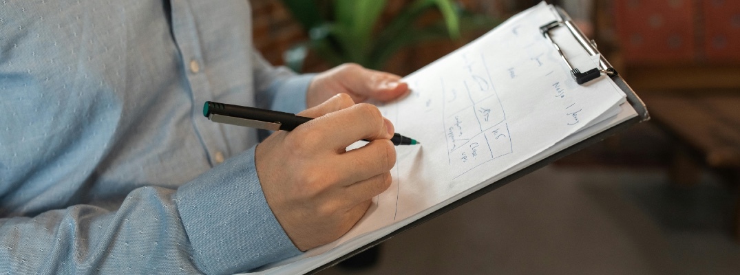 A worker in a button down top writes on a document on a clipboard